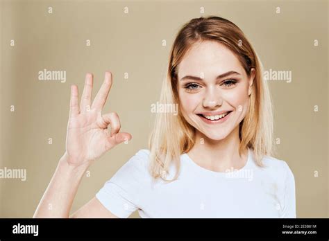 Cheerful Blonde Woman In A White T Shirt Gestures With Her Hand Emotions Beige Background Stock