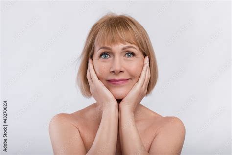 Portrait Of Charming Nude Senior Lady Touching Her Face Over Light Studio Background Stock Photo