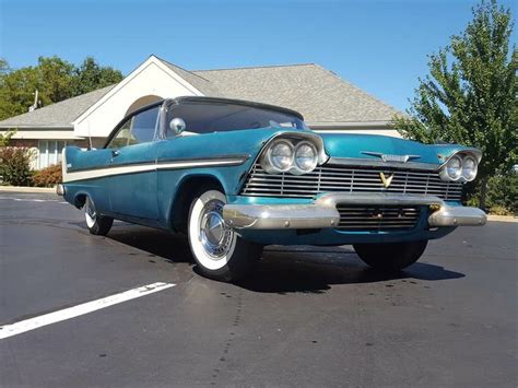 An Old Blue Car Parked In A Parking Lot Next To A White And Gray House