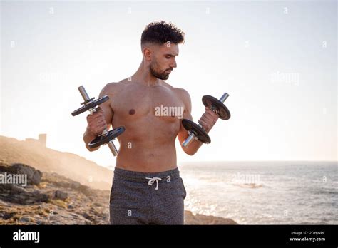 Handsome Male Athlete With Naked Torso Doing Exercises With Dumbbells While Standing Against