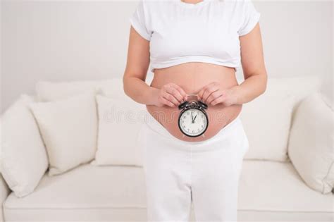 A Pregnant Woman With A Naked Belly Holds An Alarm Clock Intended Date Of Birth Stock Photo