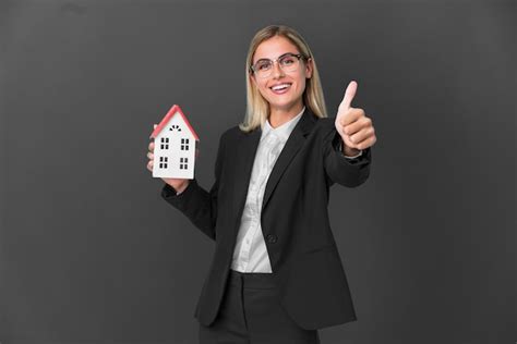Fille Blonde Uruguayenne Tenant Un Jouet De Maison Isol Sur Fond Noir Avec Les Pouces Vers Le