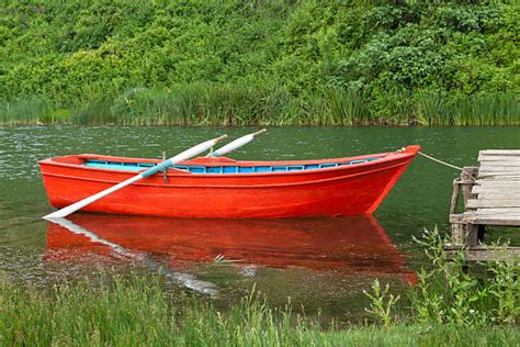 A small empty red row boat docked in a lake - Photos by Canva