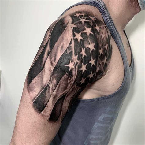 American flag upper arm tattoo. The tattoo depicts an American flag to be beneath the owner’s skin with the words “Made in the U.S.A” appearing above and below it. This is an ideal American flag tattoo idea for the men who have big biceps and arms. The tattoo depicts the American flag drawn around a man’s biceps in black and white. The flag appears to be flapping in ... 