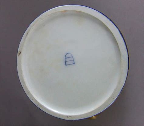 The first mark used by the Royal Porcelain Manufactory in 1744 was actually a line drawing of the outline of a shield. But when turned upside down, it looked like a beehive. Collectors today call ...