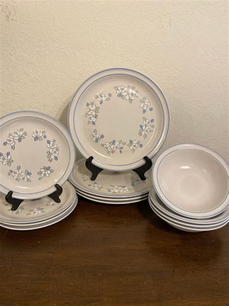 Chantilly Fleur de Lune Stoneware Hearthside Six Piece Place Setting for Eight White Pink Floral Blue Trim Saucers and bowls are solid cream with blue stripe. Cups have flowers on one side only. Set includes 8 each of the following: Dinner plates 10.75 diameter Small plates 7.75” diameter Cereal.
