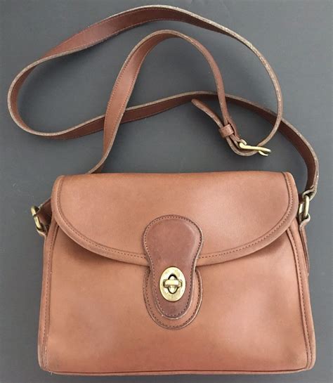 Coach british tan. Vintage Coach Rambler Shoulder Bag British tan leather with brass hardware Roomy interior, zippered pocket, outer slip pocket covered by a flap and secured with a turnlock Adjustable 42” strap at last hole Strap drop: 16”-19” Measures: 12”L, 10”H, 5 1/2”W Hang tag and chain Made in New York Factory, USA #335-6613 