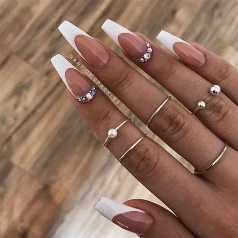 Rock a chic and glamorous style with these coffin nails featuring elegant white V-cut French tips. The nails are embellished with white 3D flowers, sparkling rhinestones as pistils, huge gems, and silver glitter on accent nails. Stylish White Borders Image courtesy of @kikinails_ebeauty. 