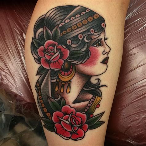First off, a traditional gypsy tattoo usually has a woman with black-colored hair, deep skin tone, and heavy makeup with quite a bit of emphasis on her eyes and lips. She usually wears a veil, with feathers, roses, and jewels on her head, and is accompanied by a crystal ball in most designs.. 