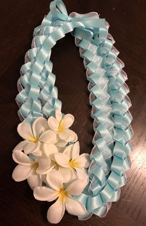 Diy graduation ribbon lei. Take the two pieces of ribbon and tie a double knot about 9-11" from one end. String both ribbons through your embroidery needle, then string one kukui nut and knot. Repeat this until you have strung four nuts. You can also double knot in between each nut if you want them to look more spaced out. 