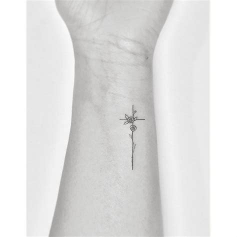 Fine line flower cross tattoo located on the wrist.