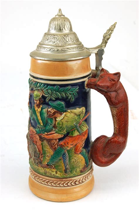 This beautiful stoneware beer stein was handcrafted in Germany by King. This new stein has a pewter lid. The handpainted relief shows forest scenes that include deer and wild boars. The handle is a fox. The text Jager's Freud Die Grune Heid wraps around the bottom of the stein. This .4 liter stein is about 8.25 inches tall.