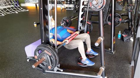 Hip thrust on smith machine. Sit on the floor with your back against a sturdy bench. Roll the barbell up over your thighs, until it is placed over your hips. Place your feet on the floor, about shoulder-width apart, with bent knees. Place your hands on the bar to stabilize it. Push the bar towards the ceiling by extending your hips. 