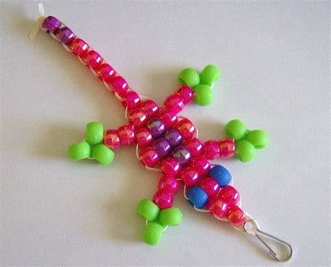 How to make a beaded animal keychain. 50 green beads; 12 yellow beads; 2 black beads; 3 yards satin cord; Metal lanyard hook; Instructions. Fold your cord in half to find the center. Use a half hitch (see detail below) to secure it to lanyard hook. Lace beads using pattern below as a guide. Finish by tying off with a double knot. Images 