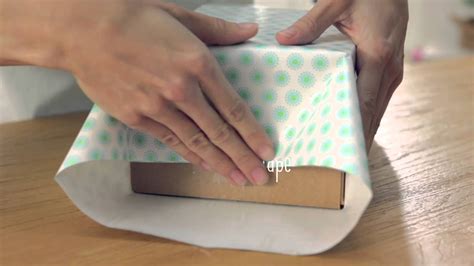 How to wrap a box with a handle. Place the base of a cardboard filing box in the center of the fabric. Next, measure and mark one inch from all sides of the box. Remove the corners of the fabric, cutting in until you reach the one-inch mark from the corners of the box. The remaining fabric should look like a large cross. Cut in one inch toward each corner of the fabric. 