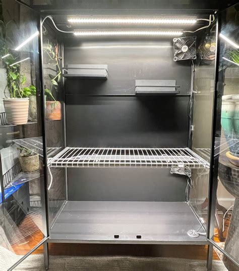 This is the Ikea Rudsta. It comes with two glass shelves, but I swapped them out for one wire shelf, leaving the bottom open for taller plants. The back of the cabinet is metal and the smaller shelves are magnetic spice racks from Amazon. There are two Barrina T5 LEDs in here, two USB fans, a heat mat, and two pots of water with LECA for ... . 