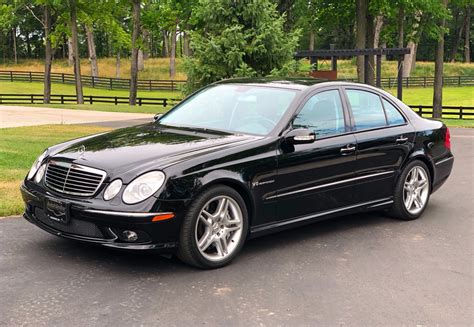 This 1999 Mercedes-Benz E55 AMG sedan is finished in white over graphite leather and is powered by a 5.4-liter V8 paired with a five-speed automatic transmission. Equipment includes AMG bodywork, a power sunroof, xenon headlights, automatic climate control, and heated and power-adjustable front seats.. 