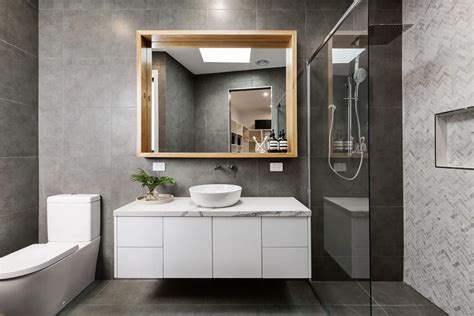 a modern taupe bathroom clad with large scale tiles, a sleek vanity that hides a washing machine, a large mirror cabinet. a modern white bathroom with a bathtub, an open timber vanity with a washing machine, a mirror and built-in shelves. a neutral bathroom with a mirror, a large vanity with sliding doors that hides a washing machine …. 
