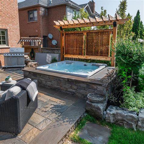 Patio hot tub. The space has a built-in fire pit and Master Spas hot tub. Make s’mores, play some music, or soak in the warm water of the hot tub. While big, this backyard feels cozy thanks to the separate seating areas and the choice of greenery. Landscape rocks and a stone wall add texture and dimension while defining the space. 