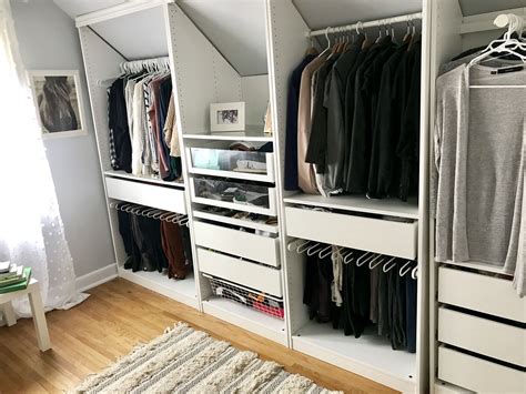 Under a sloped ceiling and in a chic walk-in closet, white flat front wardrobe cabinets adorned with brass knobs are positioned beside a linen pink board .... 