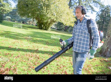 The image shows a man using a leaf blower to move some …