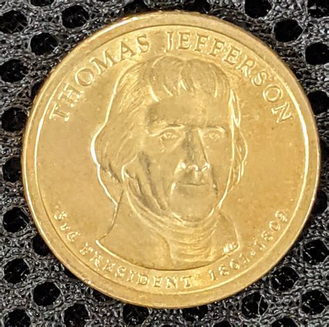 The Thomas Jefferson dollar coin features a portrait of Thomas Jefferson on the obverse, with the inscriptions “Thomas Jefferson,” “3rd President,” and “1801-1809.” The reverse of the coin features an image of the Statue of Liberty, along with the inscriptions “United States of America” and “$1.”.