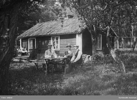 Tre män vid ett kaffebord i trädgården till en liten timrad stuga ...