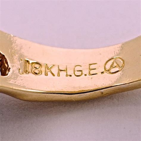 The "18kt" refers to the gold plating, indicating that it is 18-karat gold. The "G.E." stands for "Gold Electroplate" or "Gold Electroplated," indicating the plating process used to apply the gold ....