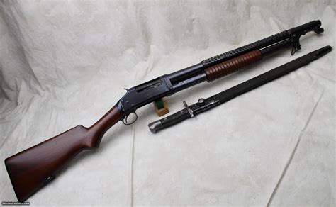 Winchester Model 97 Slide Action Trench Shotgun with Omaha Police Markings and a BayonetManufactured in 1942. The barrel is marked "OMAHA POLICE DEPARTMENT" with a 6-hole pattern heat shield, "1918" patent dates on the bayonet lug (lug notched on the left side, possibly to accommodate a non-standard bayonet), cylinder choke, 2 3/4" …