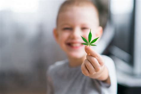 enfant souriant tenant une feuille de cannabis