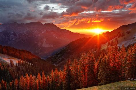 the sun is setting over a valley with trees and mountains in the